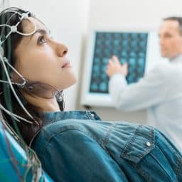 Vital procedure. Beautiful dark-haired woman lying on an examination table and undergoing electroencephalography while her doctor examining CT results