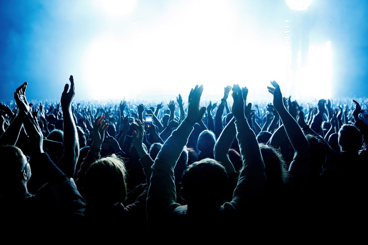 A crowd of people with raised arms during a music concert with an amazing light show.