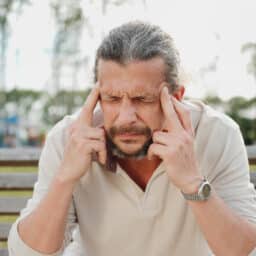 Man with tinnitus sitting on a bench massaging his temples.