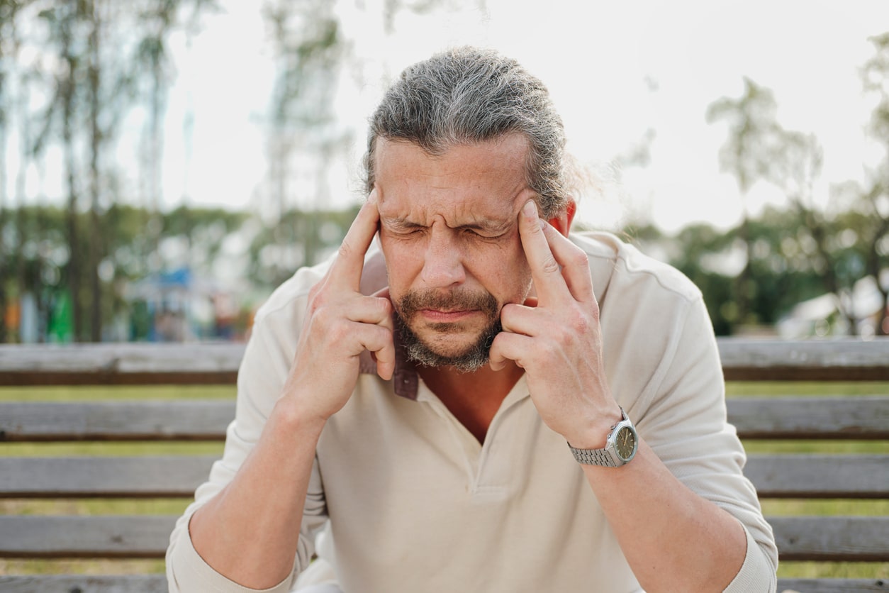 Man with tinnitus sitting on a bench massaging his temples.
