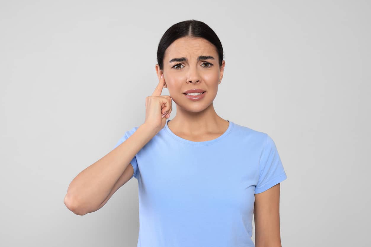 Woman with tinnitus holding her ear and looking uncomfortable.